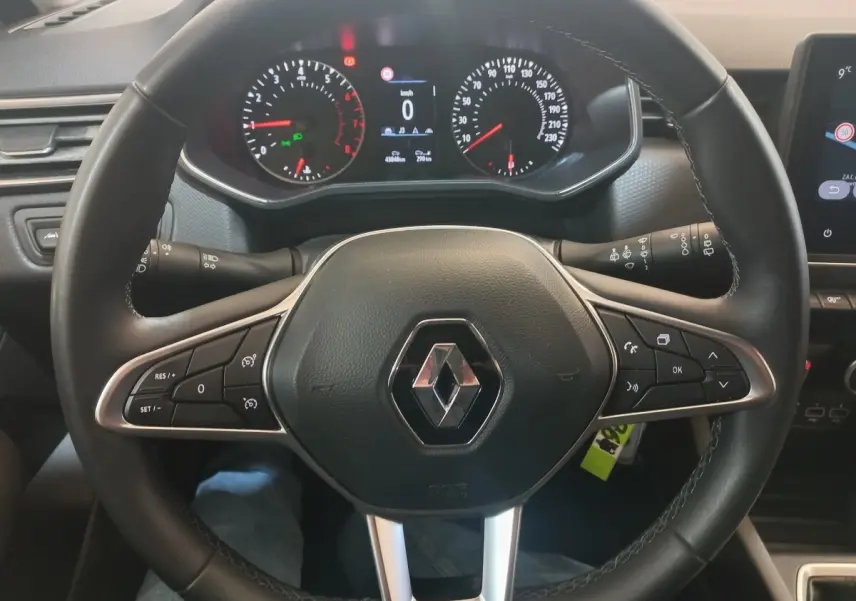 Vue rapprochée du volant en cuir synthétique noir d'une Renault Clio Business blanche, avec commandes multifonctions et tableau de bord numérique.