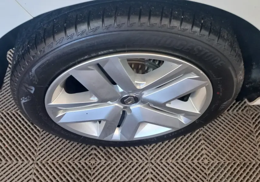 Gros plan sur la roue avant droite d’une Renault Clio blanche 2021 avec jante alliage argentée et logo Renault central.