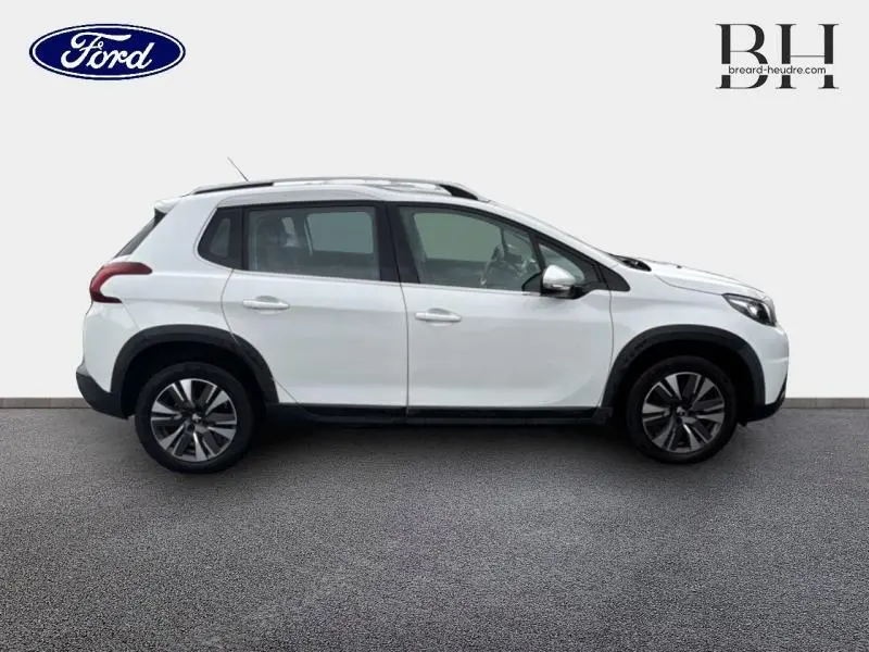 Vue de profil côté gauche d'un Peugeot 2008 blanc Banquise avec jantes alliage et barres de toit.