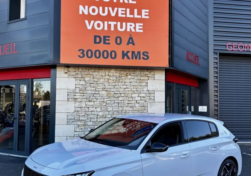 PEUGEOT 308 Hybrid blanc vue 3/4 avant droit, calandre noire et feux LED verticaux, devant un bâtiment commercial.