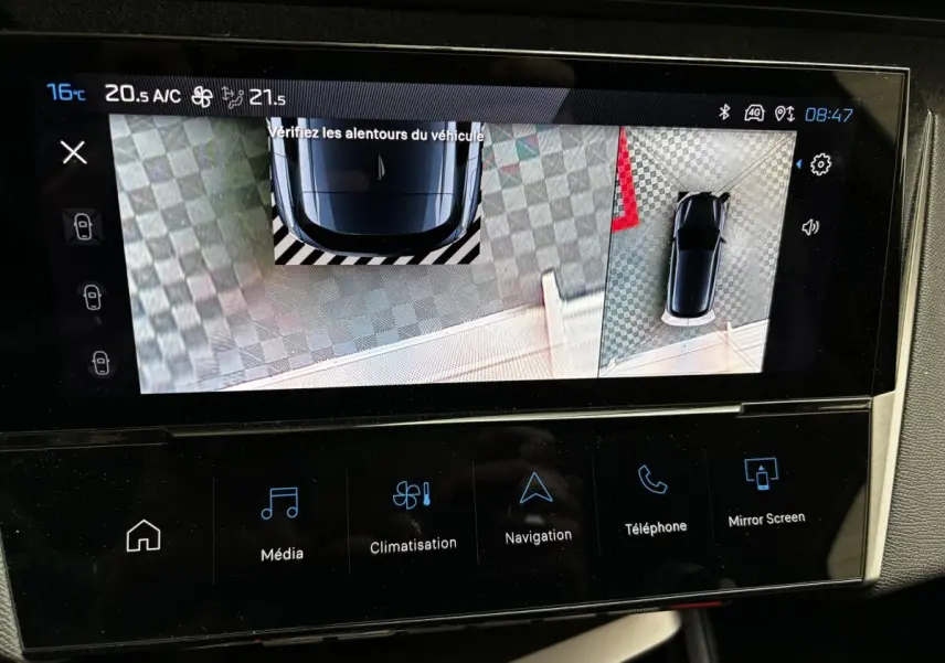 Écran tactile montrant l'aide au stationnement arrière avec vue 360° d'une Peugeot 308 blanche, tableau de bord moderne.