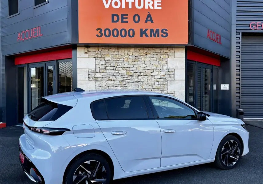 Vue latérale droite d'une Peugeot 308 Hybrid 145 e-DCS6 Allure blanche, avec jantes noires et vitres teintées.
