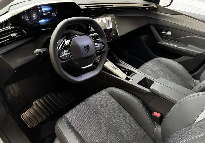 Vue intérieure côté conducteur du Peugeot 308 Hybrid 145 e-DCS6 Allure 2025, volant cuir multifonctions et écran tactile central.