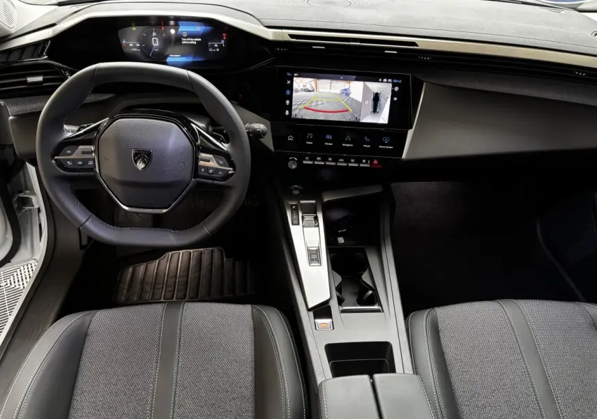 Vue intérieure avant de la Peugeot 308 Hybrid blanche, volant cuir multifonctions et écran tactile affichant la caméra de recul.