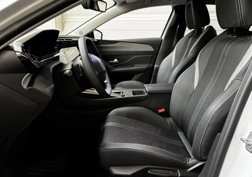 Vue intérieure côté conducteur de la Peugeot 308 Hybrid blanche, avec sièges noirs et volant cuir multifonctions.