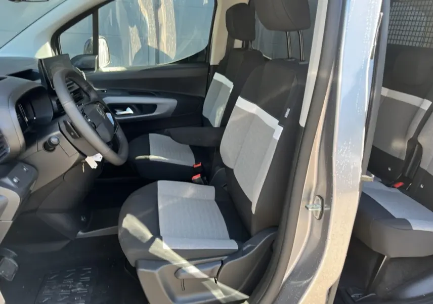 Vue intérieure côté conducteur du Citroën Berlingo gris Artense 2025, montrant les sièges tissu bicolores et le volant cuir multifonctions.