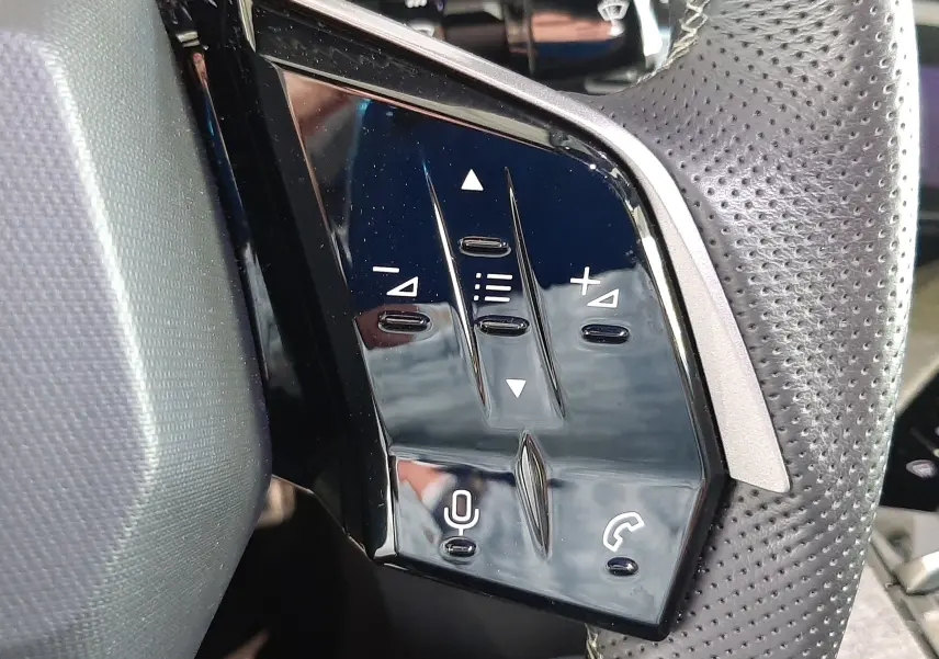 Gros plan sur les commandes tactiles noires du volant perforé du Peugeot 3008 Hybrid 2025, avec boutons de volume et appel.