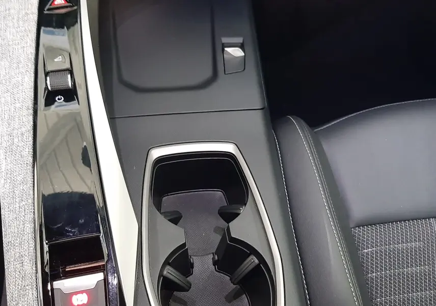 Vue rapprochée de la console centrale du Peugeot 3008 1.2 Hybrid 145ch GT 2025, avec porte-gobelets et bouton frein à main électrique.