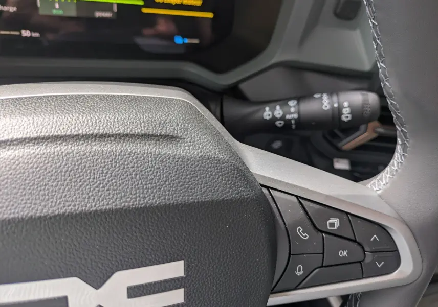 Gros plan sur le volant du Dacia Bigster Hybrid 155 Extreme avec commandes intégrées, intérieur gris et écran digital partiel visible.