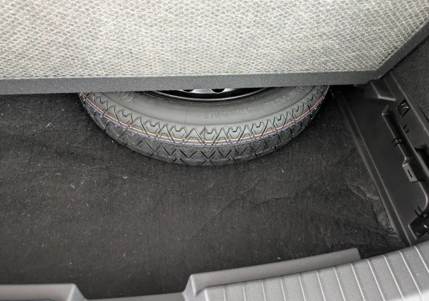 Gros plan sur la roue de secours dans le coffre du Dacia Bigster Hybrid 155 Extreme, tapis noir visible.