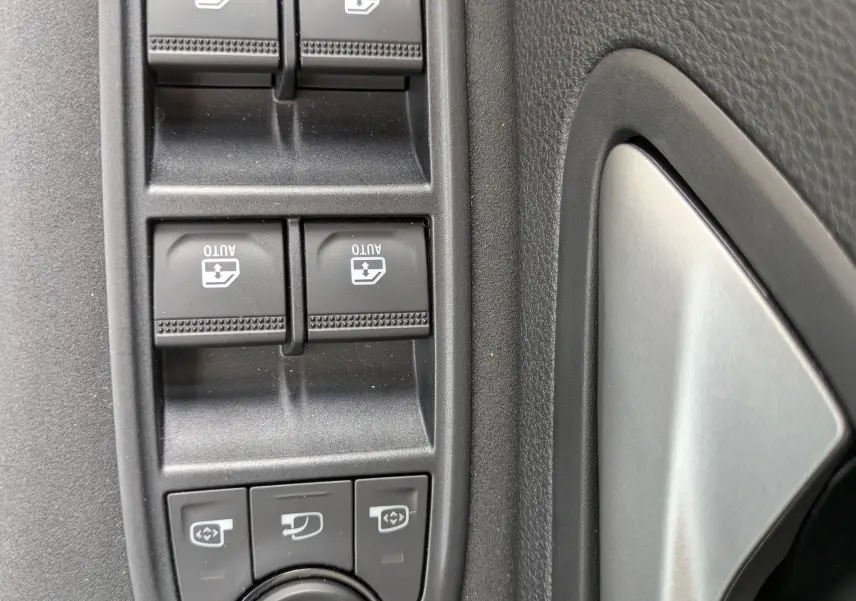 Gros plan sur les commandes de lève-vitres et réglage des rétroviseurs côté conducteur du Dacia Bigster Hybrid 155 Extreme.