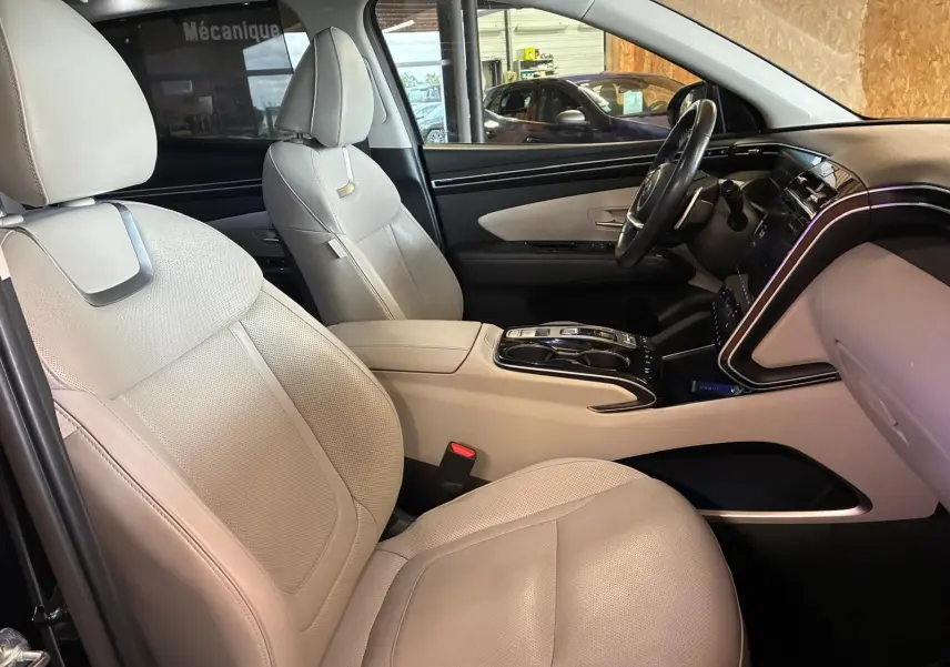 Vue intérieure côté conducteur du Hyundai Tucson 1.6 T-GDI Hybrid 230 Executive 2022 avec sièges cuir beige et tableau de bord noir.