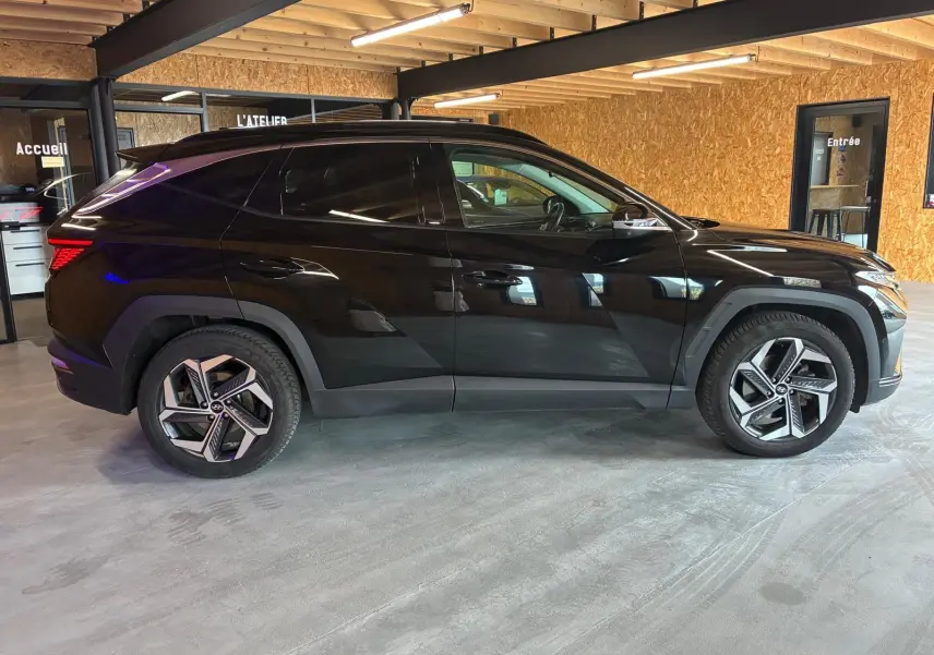 Vue latérale droite d'un Hyundai Tucson noir 2022 hybride avec jantes alliage et lignes anguleuses marquées.