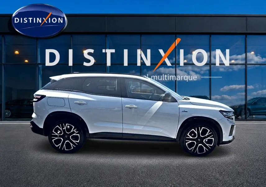 Profil droit d’un Renault Austral blanc nacré 2026 avec jantes alu noires et toit noir devant une vitrine Distinxion.