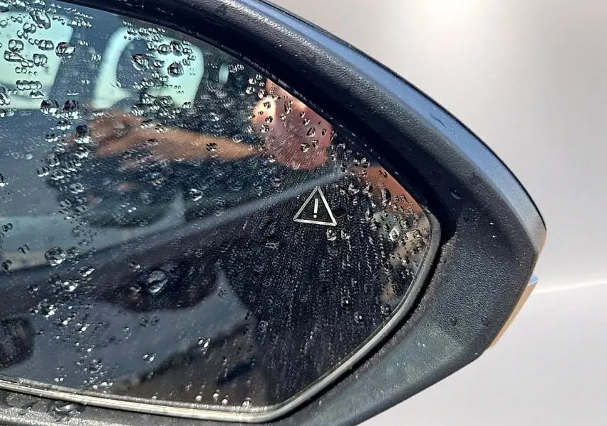 Gros plan sur le rétroviseur droit noir du Hyundai Tucson 2026 avec gouttes d'eau et symbole d'alerte visible.