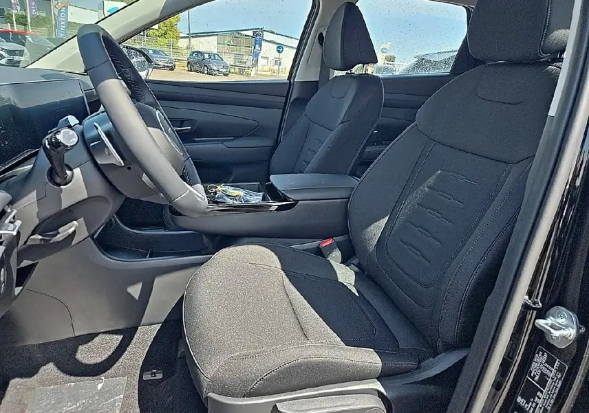 Vue intérieure côté conducteur du Hyundai Tucson 2026 noir, sièges tissu noir et volant cuir multifonction.