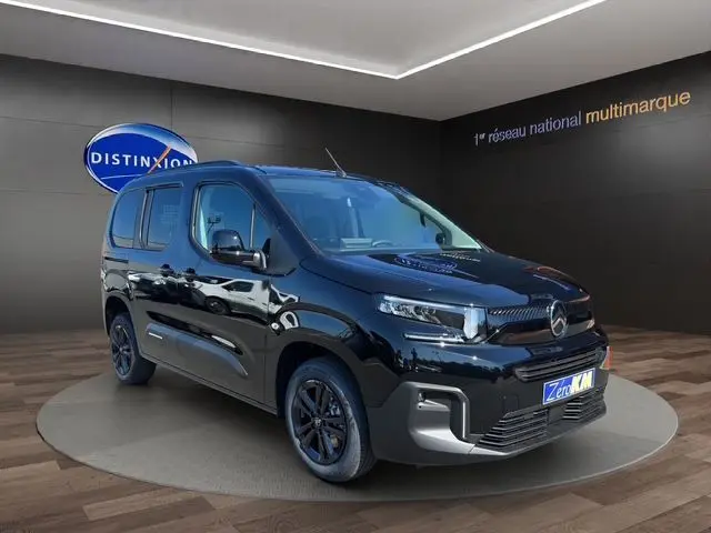 Vue 3/4 avant du Citroën Berlingo noir 2025 avec jantes noires, présenté en showroom sur fond sombre.