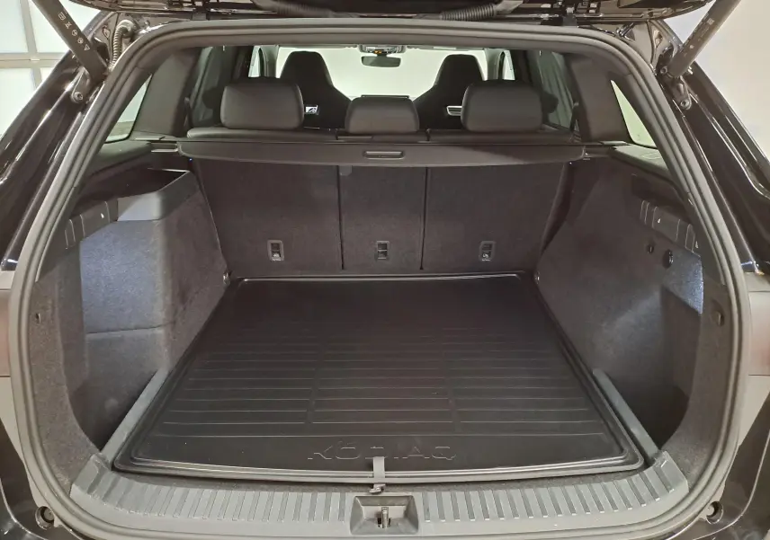 Coffre ouvert vu de l'arrière d'un Skoda Kodiaq Noir Magic Nacré avec tapis de coffre marqué Kodiaq.