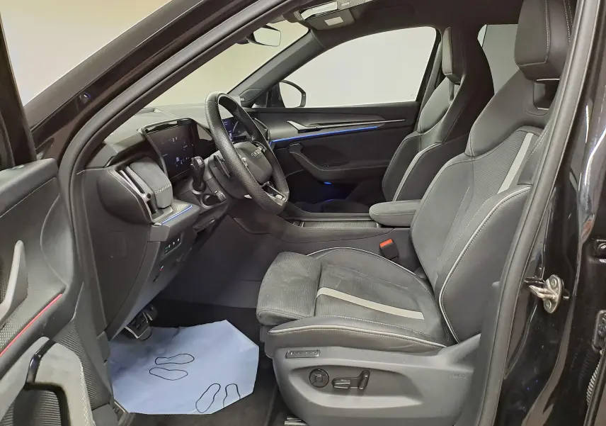 Intérieur côté conducteur du Skoda Kodiaq noir nacré 2025, sièges sport en cuir et tableau de bord avec éclairage bleu.