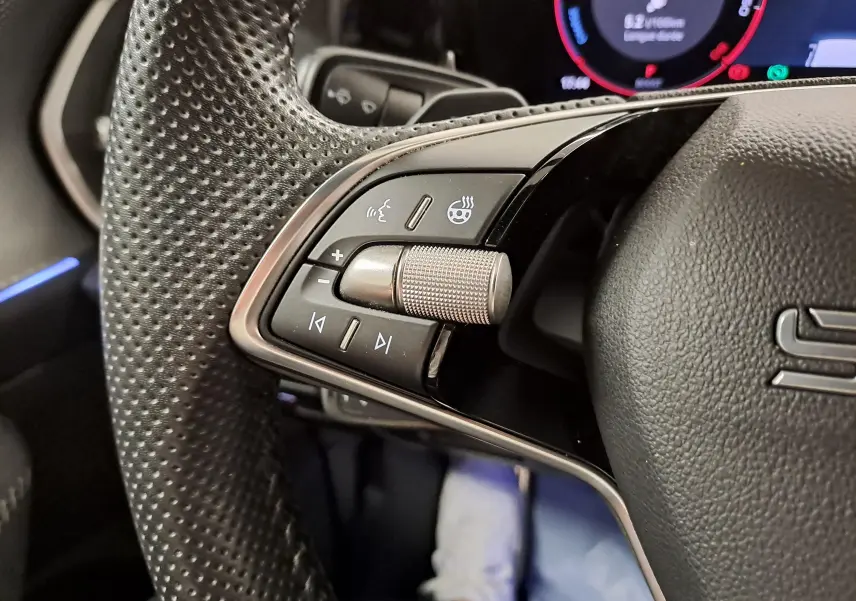 Gros plan sur les commandes gauche du volant perforé noir du Skoda Kodiaq 2025 avec molette métallique et boutons multifonctions.