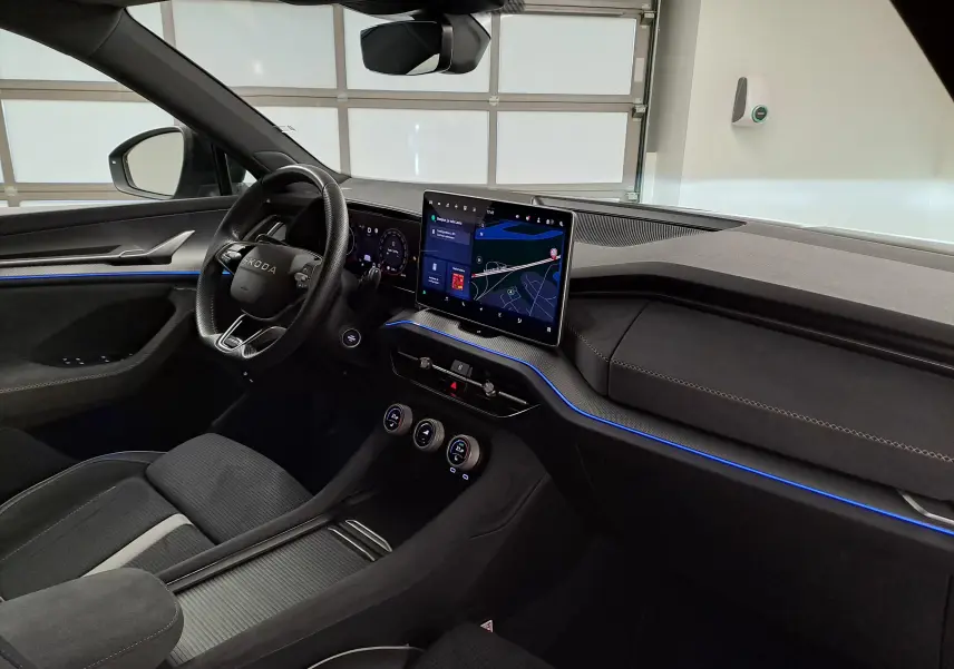 Intérieur du Skoda Kodiaq 2025 vu côté conducteur, tableau de bord moderne avec écran tactile et éclairage d'ambiance bleu.