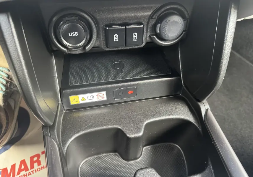 Gros plan sur la console centrale de la Suzuki Swift 1.2 Pack Hybrid 2024, montrant la prise USB, les ports de charge et le chargeur sans fil noir.