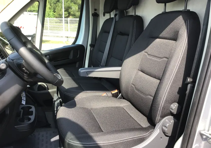 Vue intérieure côté conducteur du Peugeot Boxer Fourgon gris Artense 2025, sièges noirs avec accoudoir central.