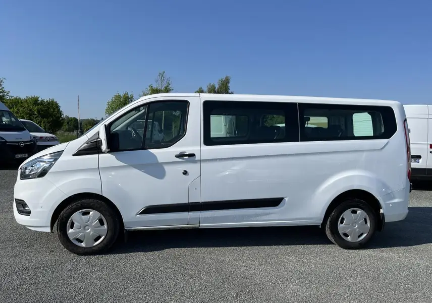 Profil côté gauche d'un Ford Transit Custom Kombi blanc, avec fenêtres latérales et jantes acier.
