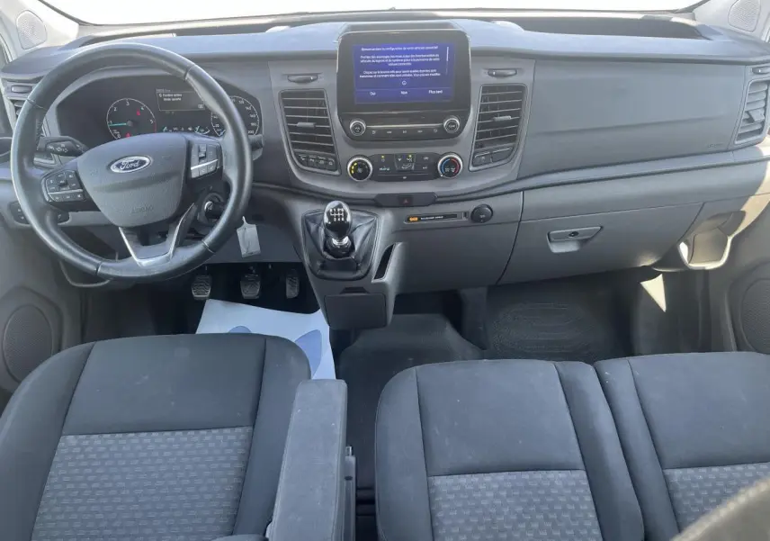 Vue intérieure avant du Ford Transit Custom blanc 2021, tableau de bord avec écran tactile et volant multifonction.
