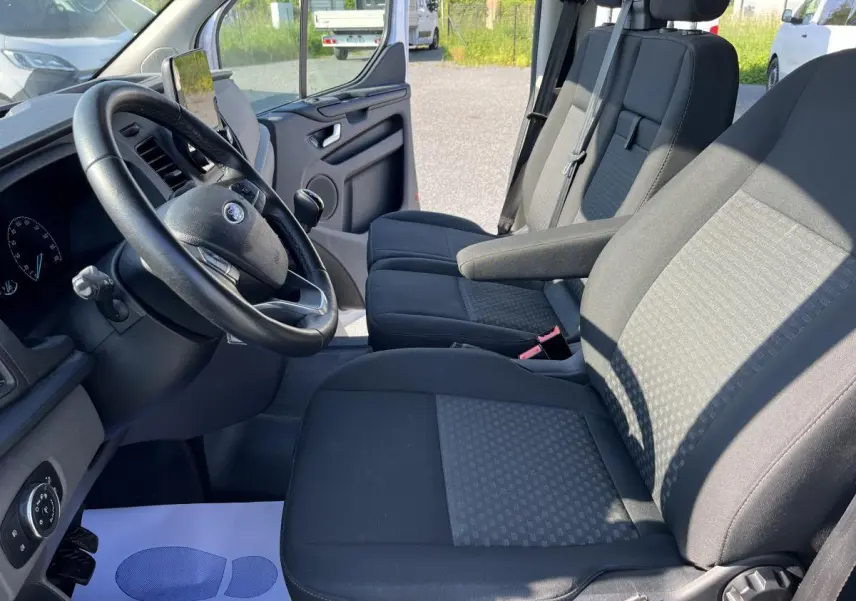 Intérieur du Ford Transit Custom blanc 2021, vue côté conducteur montrant les sièges avant et le volant cuir.