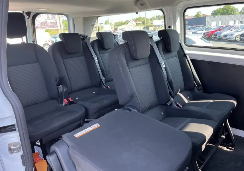 Vue intérieure côté droit du Ford Transit Custom Kombi blanc, montrant les banquettes arrière noires et les ceintures de sécurité.