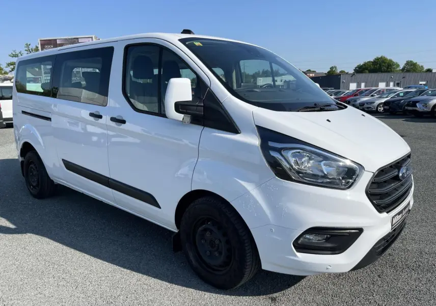 Vue 3/4 avant droite d'un Ford Transit Custom Kombi blanc avec calandre noire et jantes acier noires.