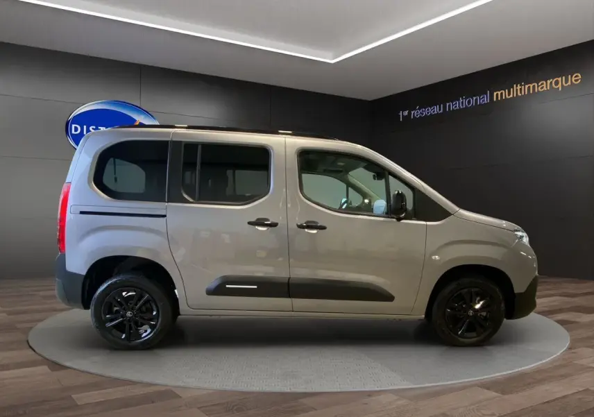 Profil droit du Citroën Berlingo gris Artense avec jantes noires et portes coulissantes visibles en intérieur showroom.