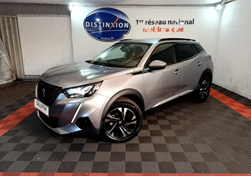Peugeot 2008 gris clair en 3/4 avant droit, avec jantes noires et toit noir dans un showroom intérieur.