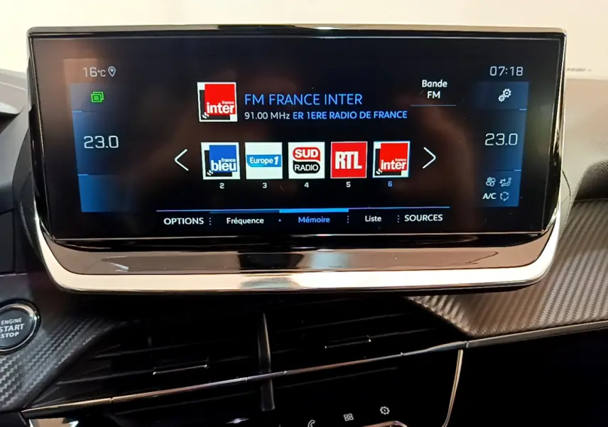 Écran tactile central du tableau de bord Peugeot 2008 gris clair, affichant les radios FM avec commandes climatisation visibles.
