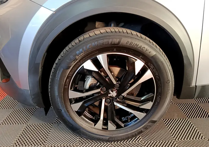 Gros plan sur la roue avant gauche d’un Peugeot 2008 gris clair avec jante alliage noire et argentée.