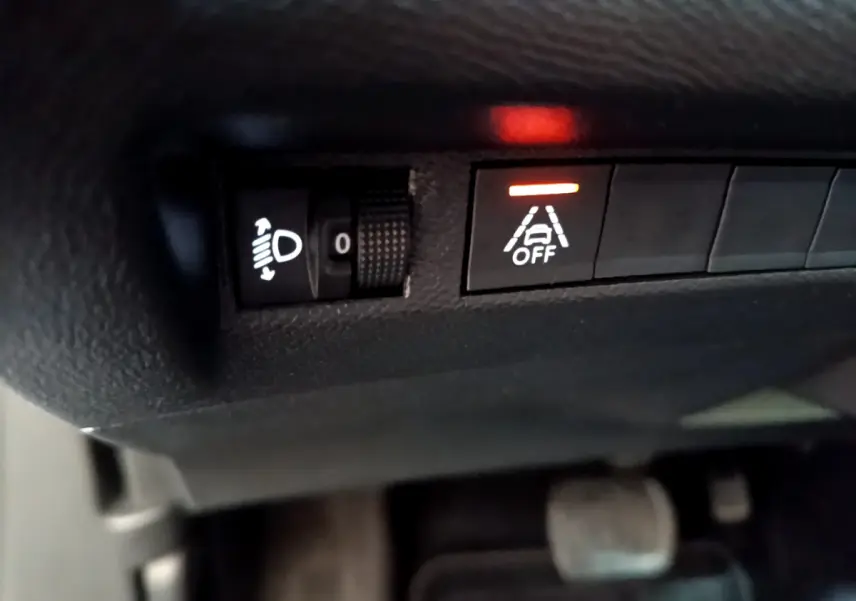 Gros plan sur les commandes d'assistance au freinage et réglage des phares dans le Peugeot 2008 gris clair 2021.
