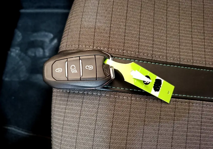 Clé de voiture Peugeot 2008 PureTech posée sur un siège tissu gris clair avec surpiqûres bleues.