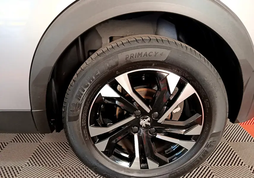Gros plan sur la roue avant gauche d’un Peugeot 2008 gris clair, jante alliage noire et argentée avec logo lion central.