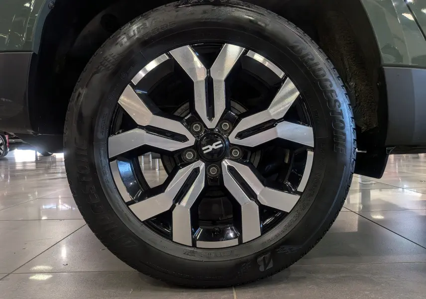 Gros plan sur la roue avant droite du Dacia Duster 2023 kaki Lichen, avec jante alliage bicolore et pneu Bridgestone.
