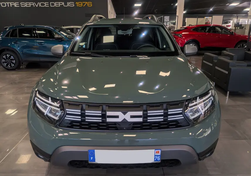 Vue frontale d'un Dacia Duster 2023 kaki lichen en showroom, avec calandre noire et détails chromés visibles.