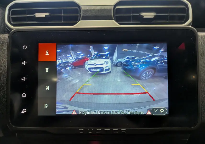Écran tactile du Dacia Duster montrant la caméra de recul avec guidage coloré dans un garage lumineux.