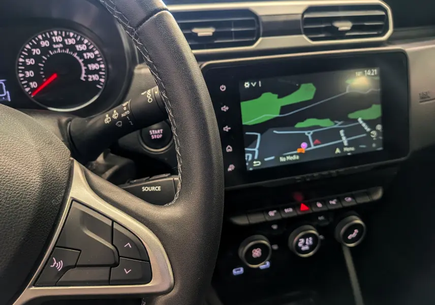 Vue intérieure du tableau de bord du Dacia Duster 2023, avec volant noir et écran tactile affichant la navigation.