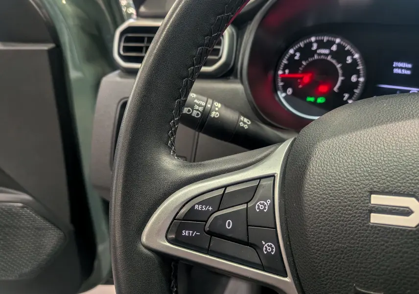 Gros plan sur le volant et le compteur du Dacia Duster 2023 kaki, montrant les commandes de régulateur de vitesse.