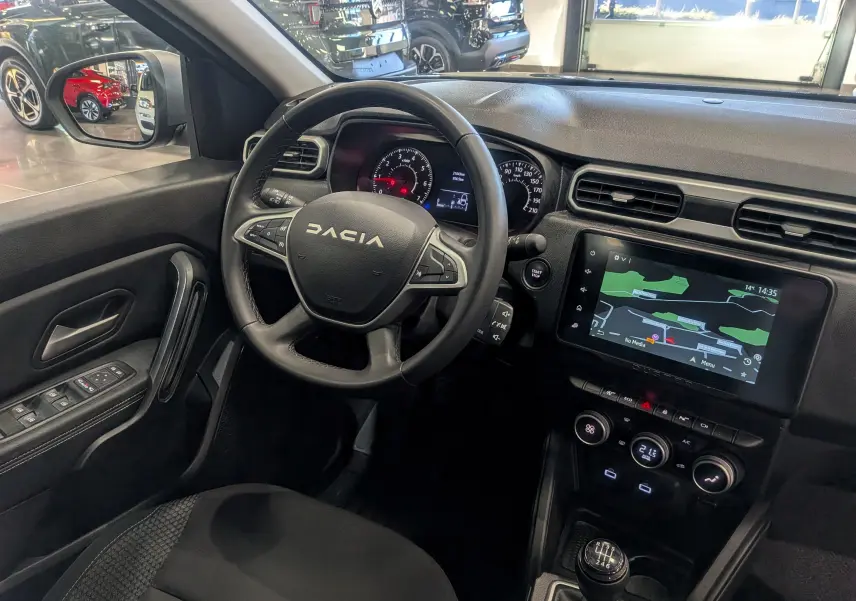 Vue intérieure côté conducteur du Dacia Duster 2023, montrant le volant, tableau de bord et écran tactile noir.