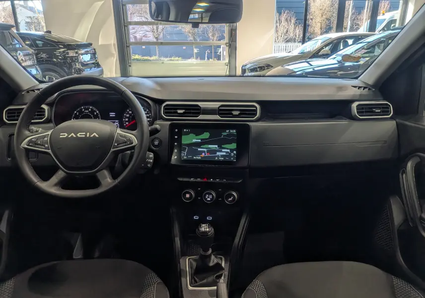 Vue intérieure avant du Dacia Duster 2023 avec tableau de bord noir, écran tactile central et volant multifonction.
