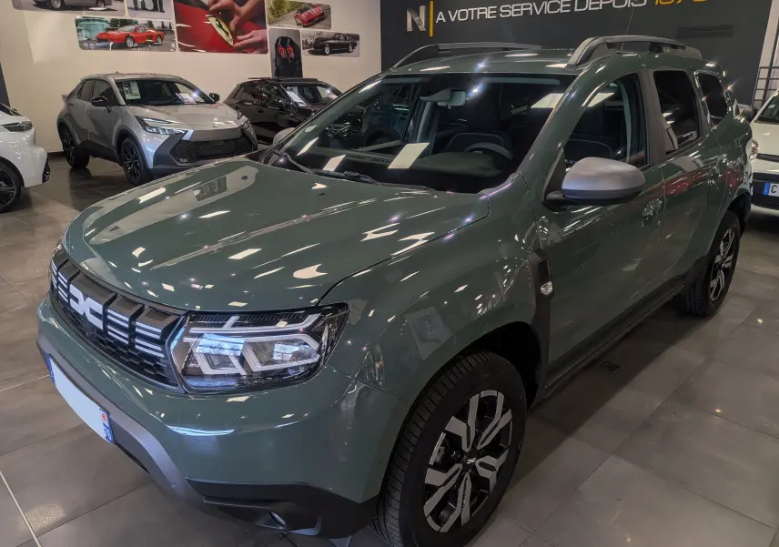 Vue 3/4 avant droite du Dacia Duster 2023 kaki lichen avec jantes biton et barres de toit visibles en showroom.