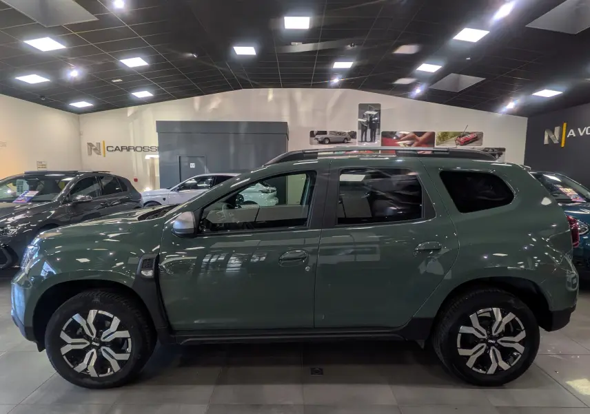 Vue de profil côté gauche du Dacia Duster 2023 kaki lichen avec jantes alliage bicolores en showroom.