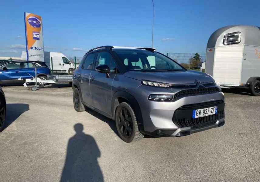 Vue 3/4 avant droit d'un Citroën C3 Aircross 2024 gris foncé avec jantes noires, stationné en extérieur au soleil.