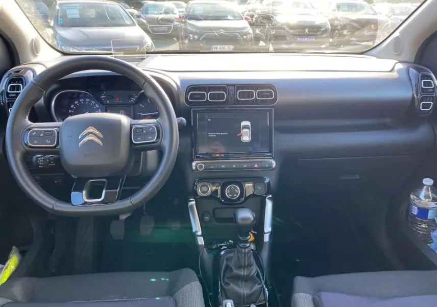Vue intérieure frontale du tableau de bord et volant noir du Citroën C3 Aircross gris foncé 2024 avec écran tactile et boîte manuelle.